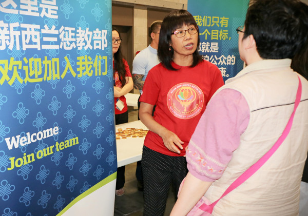 Judy talks to a member of the public beside a Corrections banner with Chinese characters that reads Welcome Join ur team